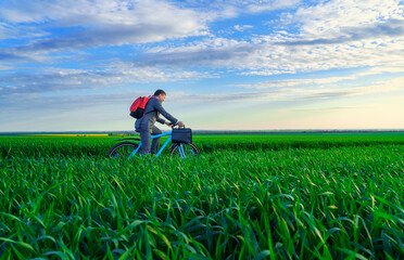 a businessman rides a bicycle with a backpack and a briefcase on a green grassy field, dressed in a business suit, beautiful nature in spring, freelance business concept