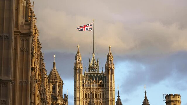 Flag of Great Britain, Palace of Westminster, Houses of Parliament in London. English tourism destination, iconic landmark, travel in England. 4k slow motion. Union Jack flag. 

