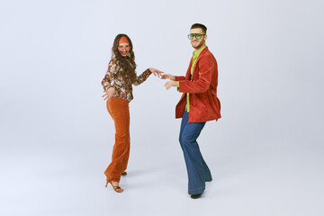 Old school party. Stylish young man and woman in colorful retro outfits dancing disco dance...