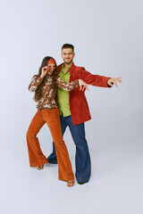 Beautiful young girl and handsome man in bright retro clothes, disco dancers posing isolated over...