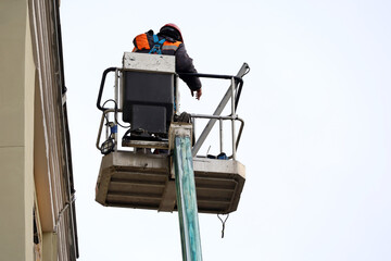 Worker in hydraulic lifting ramp repairs the building facade. Builder on lifting platform standing near the house, construction and repair works