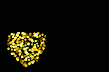 Defocused yellow circles of light in the shape of a heart with bokeh effect on a black background with copy space