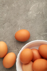 Top view of raw brown eggs on plate on grey background.