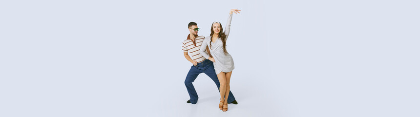 Young beautiful girl in silver dress and stylish man dancing disco dance isolated over grey studio...