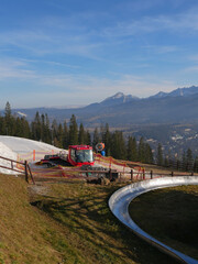 Zakopane, Poland - 01 01 2023 : A snowplough is parked in a valley without snow. Tatras mountains in background.