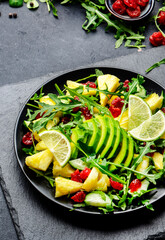 Vegan pineapple salad with fresh arugula, avocado and dried cranberry on black kitchen table, top view. Healthy eating, clean diet food, weight loss dish