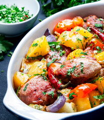 Baked turkey drumsticks fillet with potatoes, paprika, onions, herbs and spices in baking dish, black table background, top view