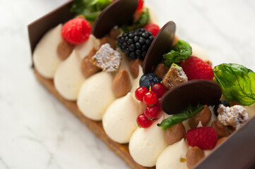 Top view of vanilla namelaka cake with chocolate circles, mocha mousse, raspberries, blackberries,...