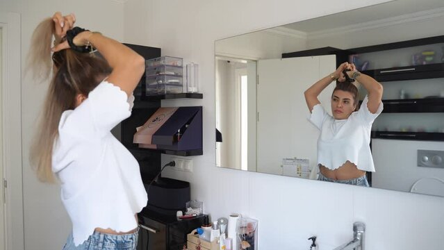 Brazilian woman combing hair, do hairstyle in bathroom with hairbrush and band. Female morning routine. Soft focus