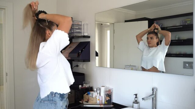 Arabian woman combing hair, do hairstyle in bathroom with hairbrush and band. Female morning routine. Soft focus