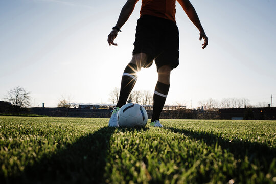 Low section of man playing soccer on grassy field against clear sky during sunset