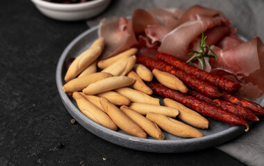 Spanish jamon, Sticks of Chorizo and picos bread sticks on the grey plate and dark table. Tapas concept