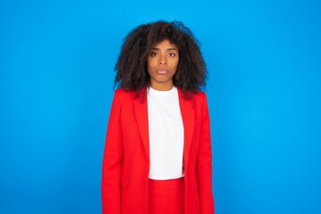 Joyful young businesswoman with afro hairstyle wearing red over blue background looking to the...