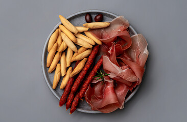 Plate with Spanish jamon, sticks of chorizo and picos bread sticks on the grey background. Tapas concept. flaty lay