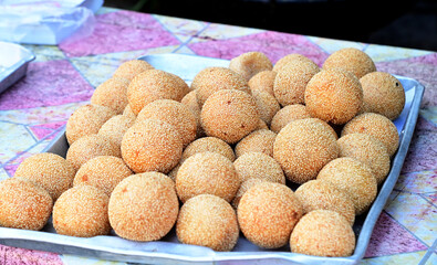 Closeup of Golden Fried Sesame Balls (Thai dessert) placed on a silver metal tray for street food at Thailand. Healthy food concept, selective soft focus.