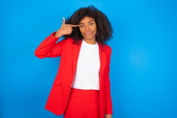 Unhappy young businesswoman with afro hairstyle wearing red over blue background curves lips and...