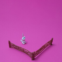 White rabbit in center with fence on a pink background with copy space. A minimalist Chinese New Year composition.