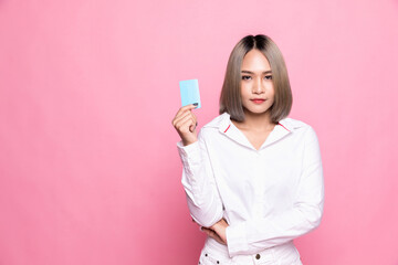 Shopping concept. Young Asian woman smiling and showing plastic credit card, paying contactless, standing over pink background