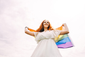 Woman with rainbow flag on sky background.