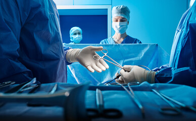 Surgeons performing surgical procedure on patient with surgical scissors inside operating room. Surgical team - 567330912