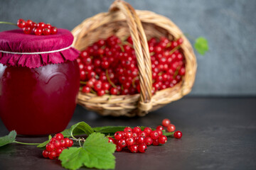 Fresh red currants in a basket and a glass with currant jam on dark background