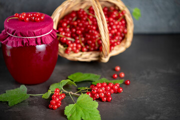 Fresh red currants in a basket and a jar of red currant jam on a dark background