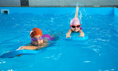 Two little girls having fun in pool learning how to swim using flutter boards
