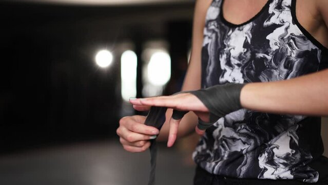 Athletic slim woman wrapping hands with boxing bandages at gym. Female athlete preparing for karate in fitness center. Sport, active lifestyle concept. Strong independent woman concept. Feminist