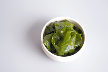 Fresh seaweed wakame in white ceramic bowl on white background.
