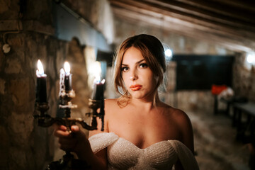 Portrait of beautiful bride holding candle in the castle at night.Portrait of beautiful bride holding candle in old stone rustic interior at night.