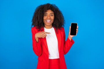Excited young businesswoman with afro hairstyle wearing red over blue background holding and...