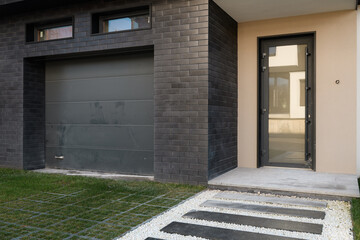 black garage door, entrance to the house, white stone and green grass