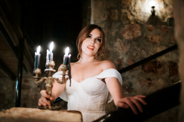 Portrait of beautiful bride holding candle in the castle at night.Portrait of beautiful bride holding candle in old stone rustic interior at night.