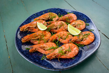 Shrimp sauteed with garlic and oil in a dark blue dish on a green painted wooden table. Brazilian food widely consumed on the coast.