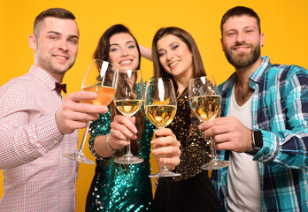 two young men and two beautiful women smiling with glasses of champagne in their hands on a yellow background