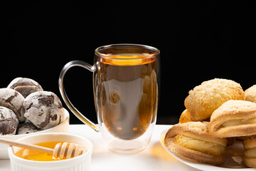 Tea with honey with cocoa cookies and cakes with creamy filling on a black background.