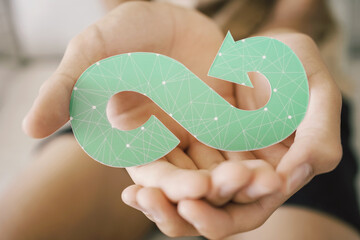 Hands holding green infinity arrow symbol, circular economy, sustainable and responsible business...