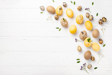 Festive Easter background. Yellow and brown Easter Eggs with flowers on a white wooden table. Greeting card with place for text. Top view.