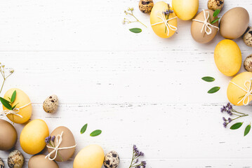 Festive Easter background. Yellow and brown Easter Eggs with flowers on a white wooden table. Greeting card with place for text. Top view. - obrazy, fototapety, plakaty