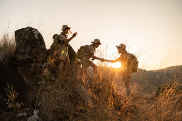 Asian boy scouts help pull up from the cliff. Unity and teamwork building concept.