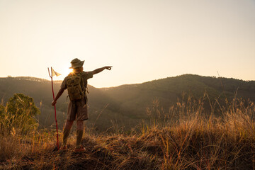 Asian Boy Scout standing on cliff with meadow Scout students point their finger at the target showing their ability to conquer the target near sunset.