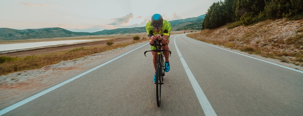 Fototapeta premium Full length portrait of an active triathlete in sportswear and with a protective helmet riding a bicycle. Selective focus 