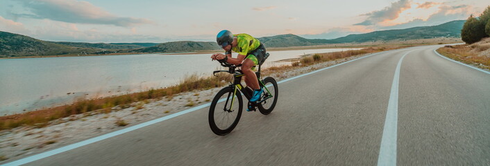 Fototapeta premium Full length portrait of an active triathlete in sportswear and with a protective helmet riding a bicycle. Selective focus 