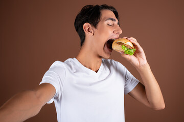 Portrait of a young student with a slice of pizza. Break for a snack. A man in a white t-shirt on a brown background.