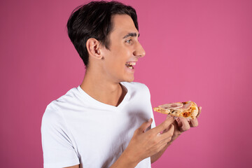 Portrait of a young student with a slice of pizza. Break for a snack. A man in a white t-shirt on a pink background.