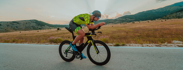 Fototapeta premium Full length portrait of an active triathlete in sportswear and with a protective helmet riding a bicycle. Selective focus 