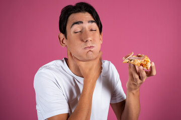 Portrait of a hungry guy in a white shirt with a piece of pizza. Pink background. Fast food.