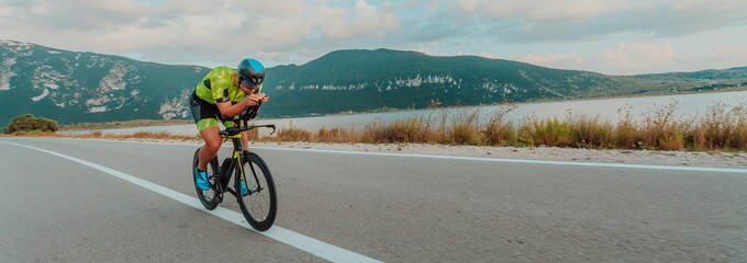 Fototapeta premium Full length portrait of an active triathlete in sportswear and with a protective helmet riding a bicycle. Selective focus 