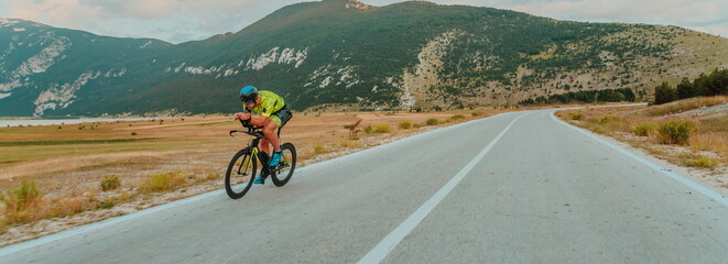 Fototapeta premium Full length portrait of an active triathlete in sportswear and with a protective helmet riding a bicycle. Selective focus 