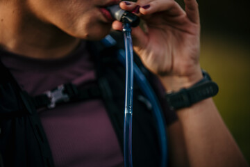 Thirsty female trail runner drinking water from hydration packs. Focus on sipping water.